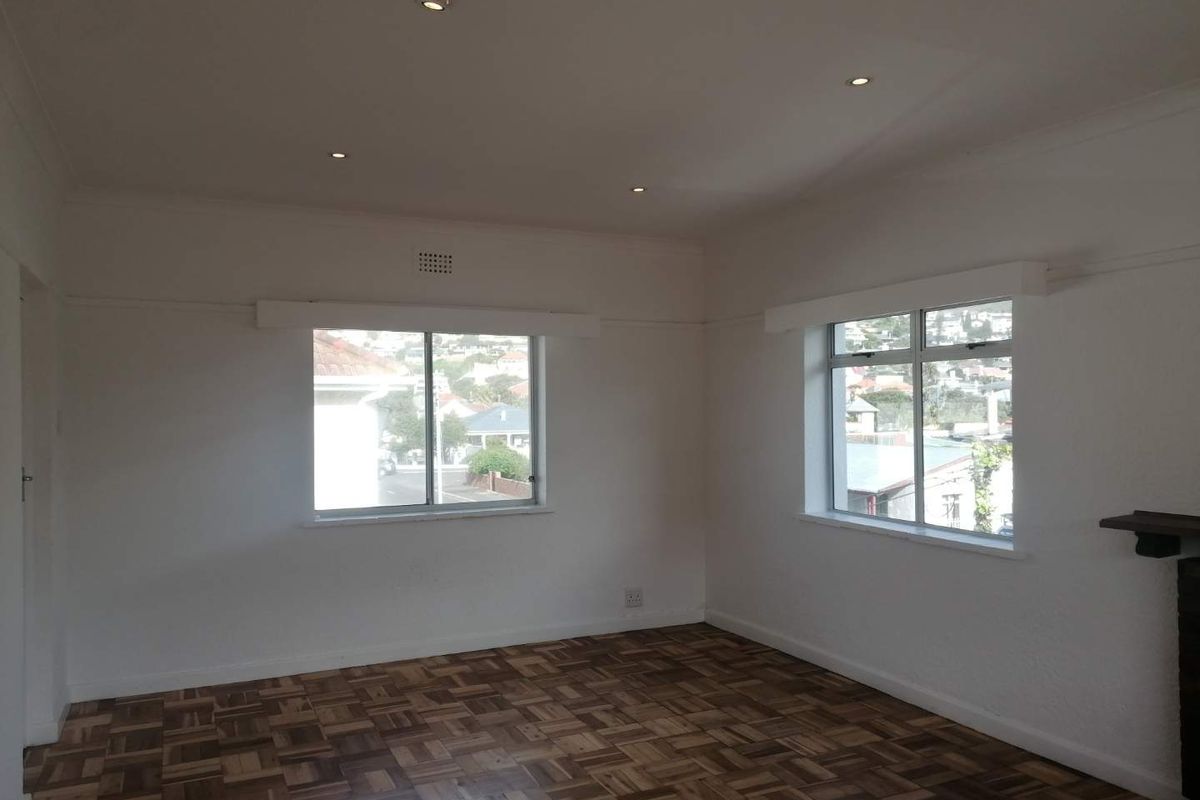 A bright, empty living room featuring classic parquet flooring, recessed downlighting, and large windows offering a pleasant neighborhood view.