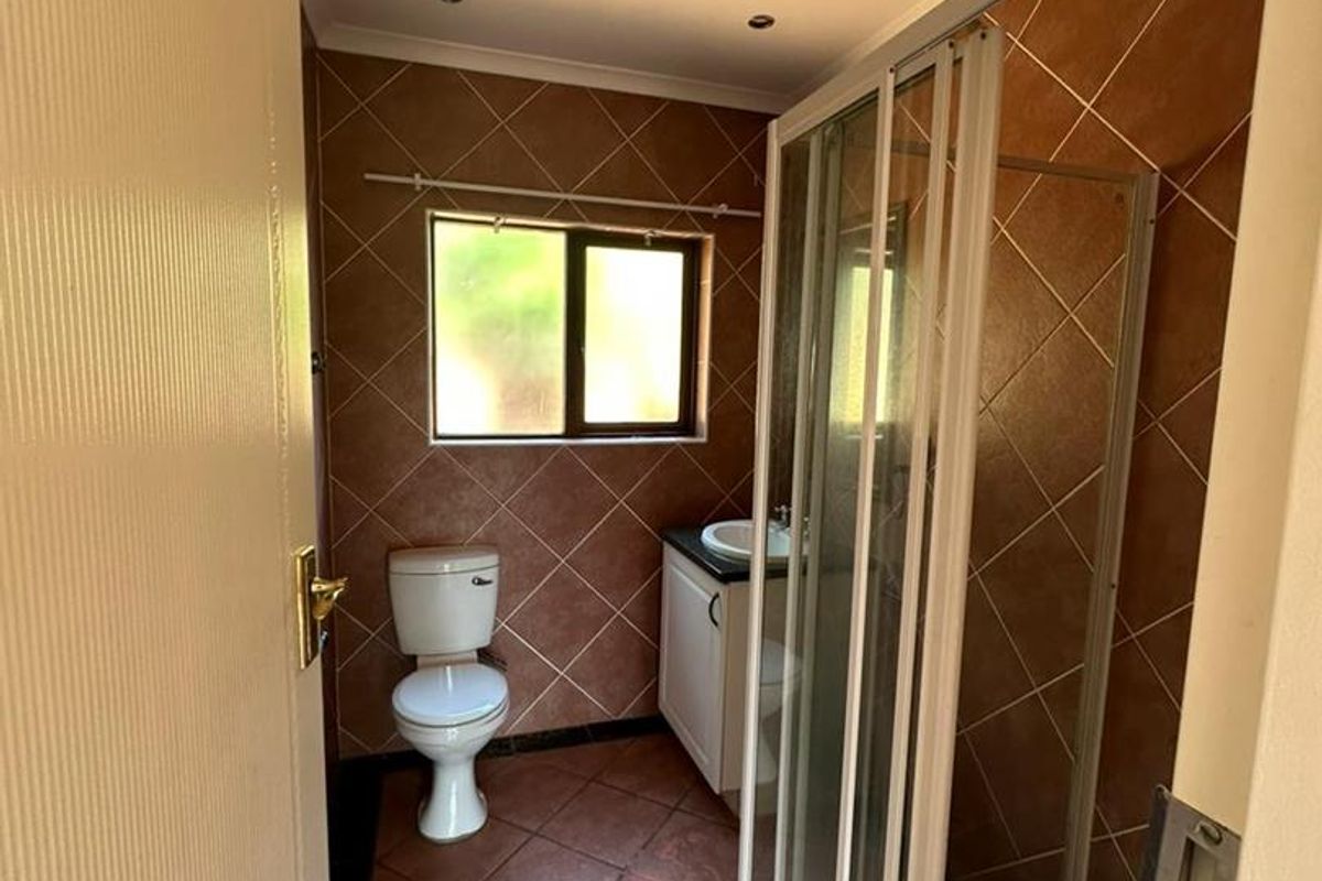 A functional bathroom featuring a shower enclosure, toilet, and vanity basin with tiled walls and flooring throughout.