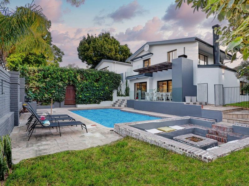 A well-maintained outdoor entertainment area featuring a swimming pool, sunken fire pit, and paved patio space adjacent to the main residence.