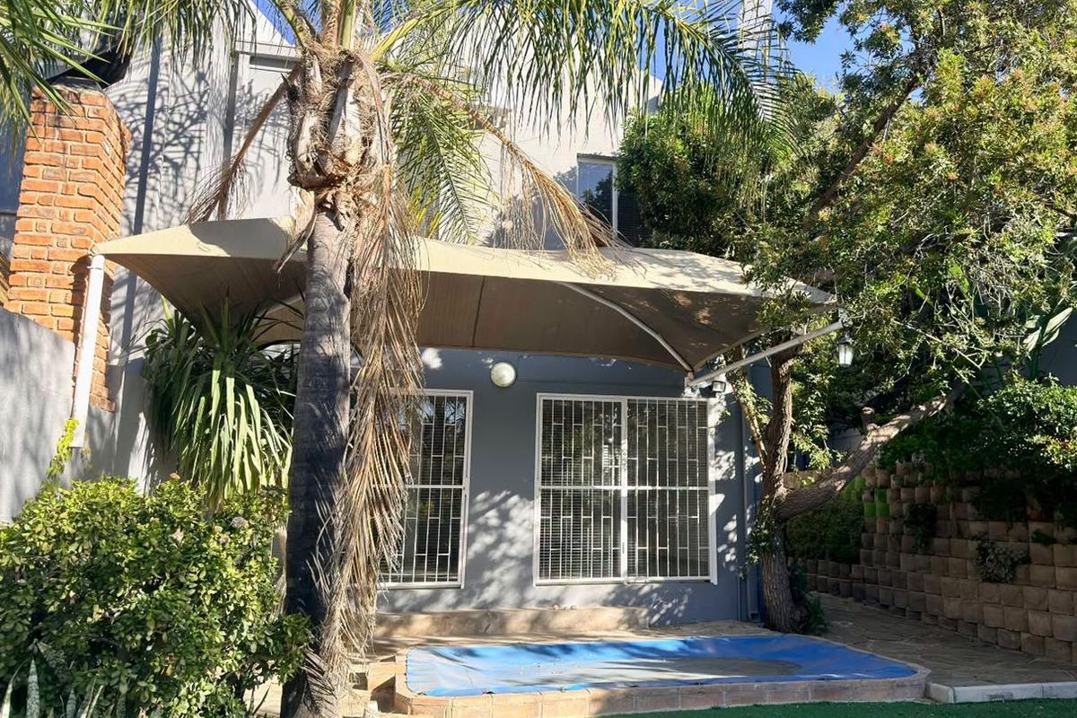 Rear exterior view of the townhouse featuring a shaded patio area, security-barred windows, and a small garden space with a retaining wall.