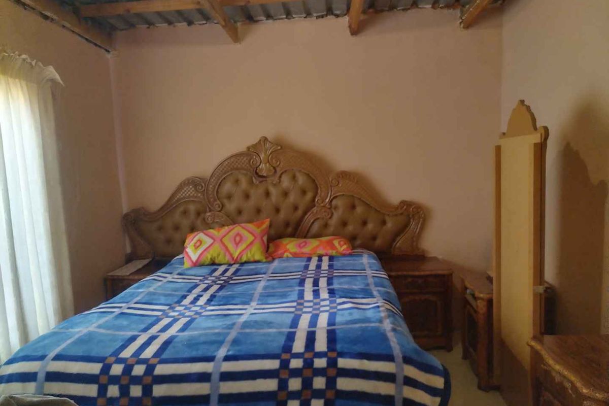 A bedroom featuring exposed timber ceiling beams and corrugated metal roofing, providing a rustic aesthetic that could be enhanced with modern finishes.