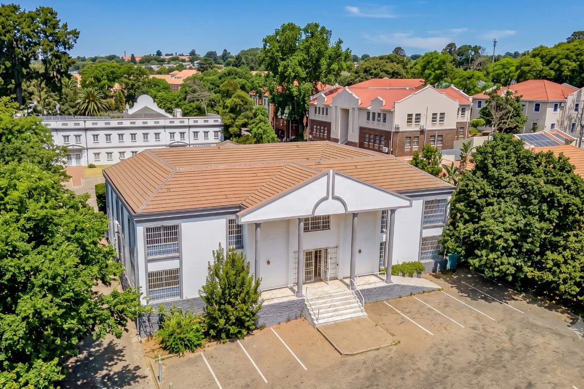 Aerial view of a commercial office building featuring a classic facade with columns, a tiled roof, and an adjacent paved parking area.