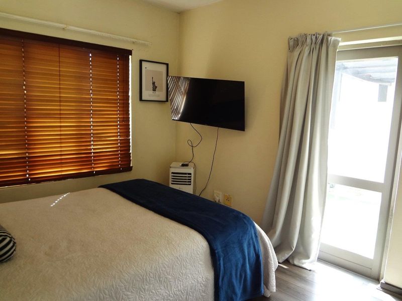 A bedroom featuring laminate flooring, venetian blinds, and a sliding glass door providing natural light and outdoor access.