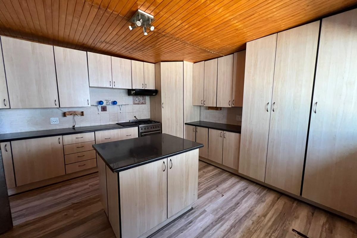 A functional kitchen featuring light wood-tone cabinetry, a central island, dark countertops, and a timber-clad ceiling, offering a clean and practical workspace.