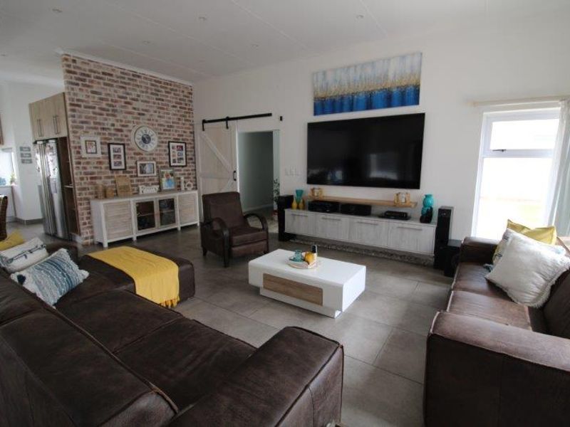 Spacious open-plan living area featuring a striking exposed brick wall, modern tiled flooring, and seamless flow into the adjacent kitchen space.