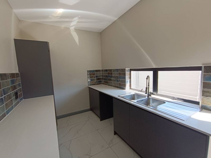 A modern, clean scullery featuring dark cabinetry, stone countertops, a double stainless steel sink, and stylish tiled splashbacks.
