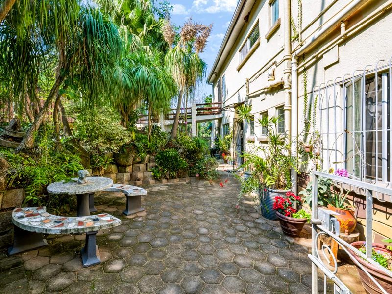 A paved rear courtyard area featuring established garden landscaping, a retaining wall, and direct access to the building exterior.