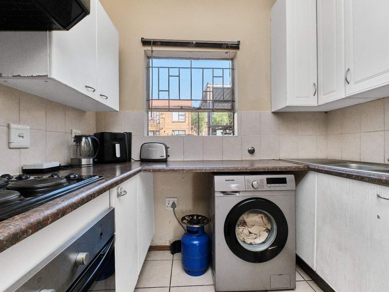 Compact kitchen featuring white cabinetry, laminate countertops, built-in oven, gas hob, and integrated laundry plumbing, with a window providing natural light.