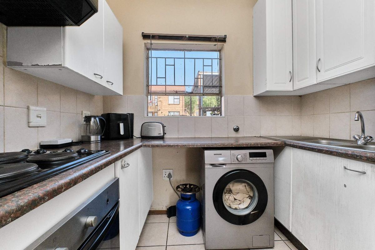 Compact kitchen featuring white cabinetry, laminate countertops, built-in oven, gas hob, and integrated laundry plumbing, with a window providing natural light.