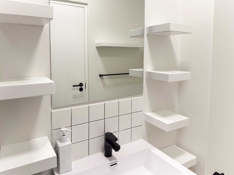 A modern, minimalist bathroom featuring a clean white basin, black fixtures, tiled splashback, and integrated wall shelving.