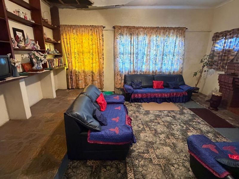Living room featuring stone flooring, built-in shelving, and a brick fireplace, currently requiring significant ceiling repairs and general refurbishment.