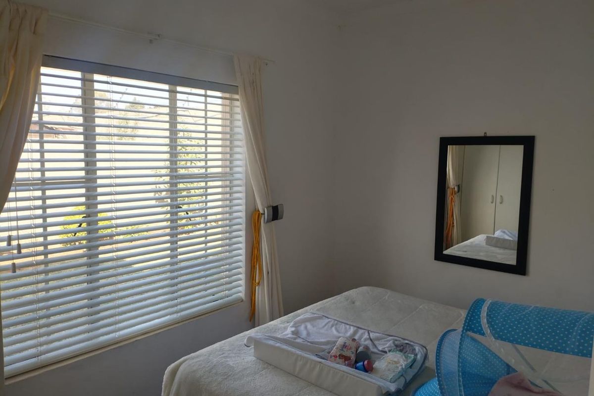 A bedroom featuring white walls, a window with venetian blinds, and a built-in wardrobe.