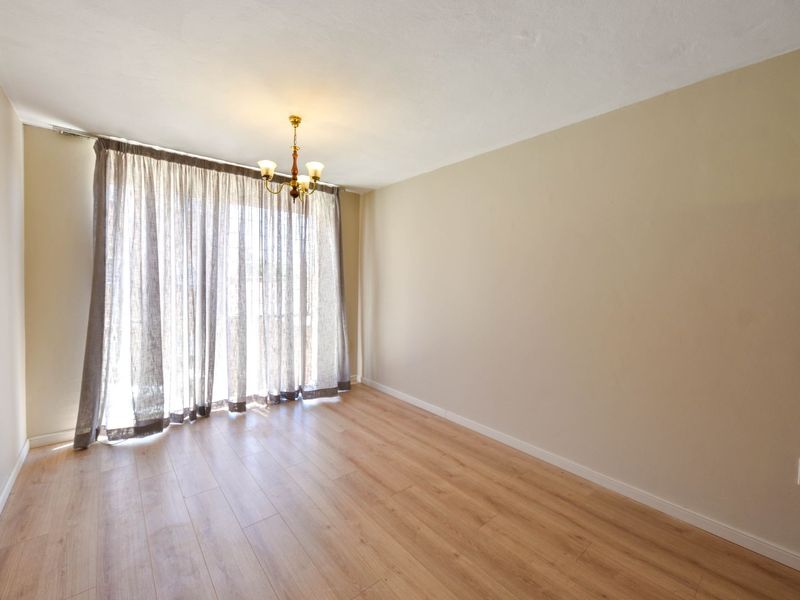 A bright and spacious living room featuring light wood-look laminate flooring, neutral walls, and a classic ceiling light fixture with large window access.