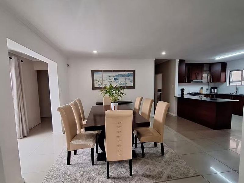 Spacious open-plan dining area seamlessly connected to a modern kitchen featuring dark wood cabinetry, granite countertops, and tiled flooring throughout.