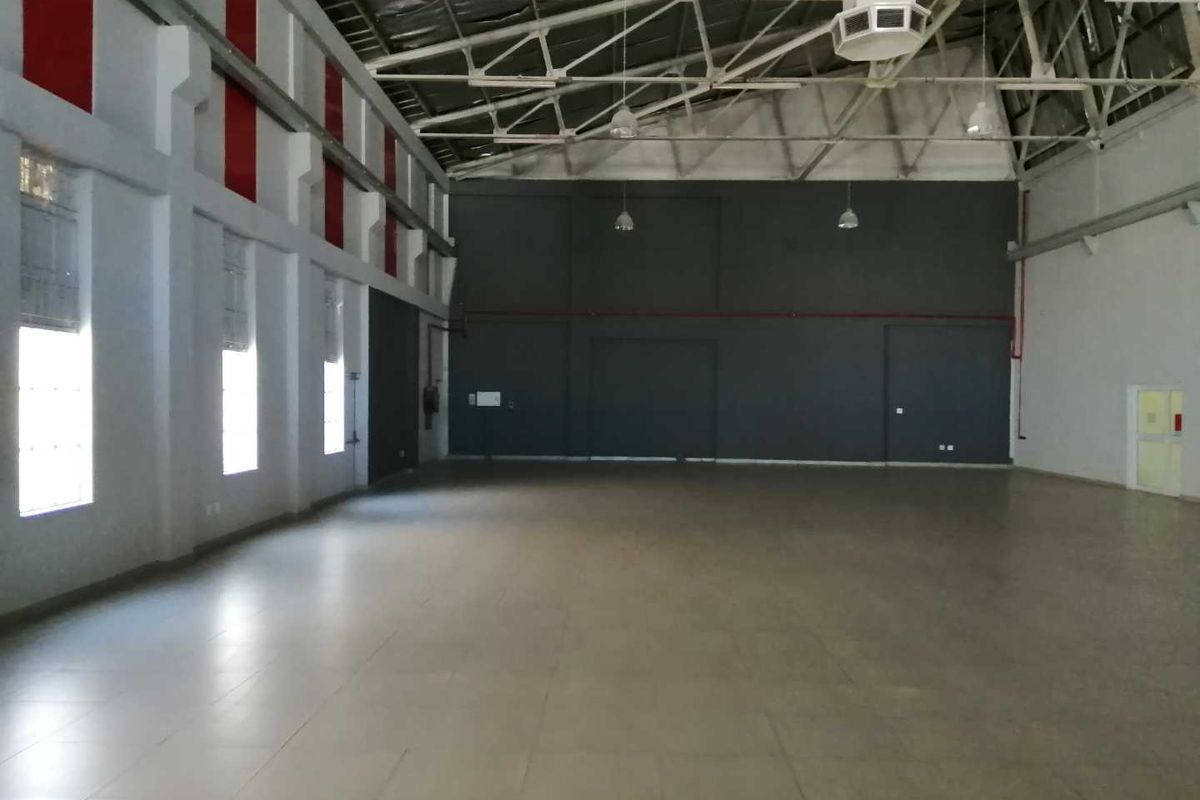 A spacious, open-plan industrial utility space featuring high ceilings with exposed steel trusses, tiled flooring, and large windows providing ample natural light.
