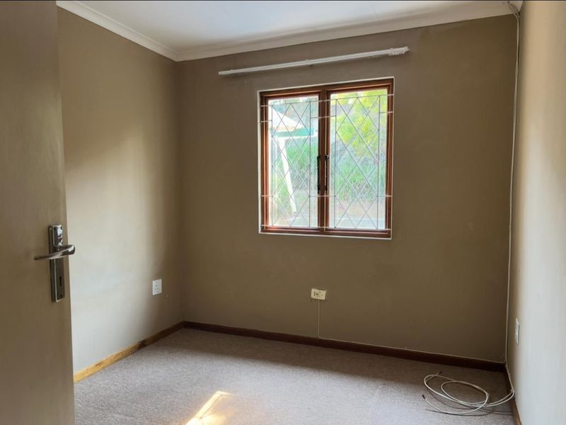 An empty bedroom featuring neutral wall tones, carpeted flooring, and a timber-framed window with security bars.
