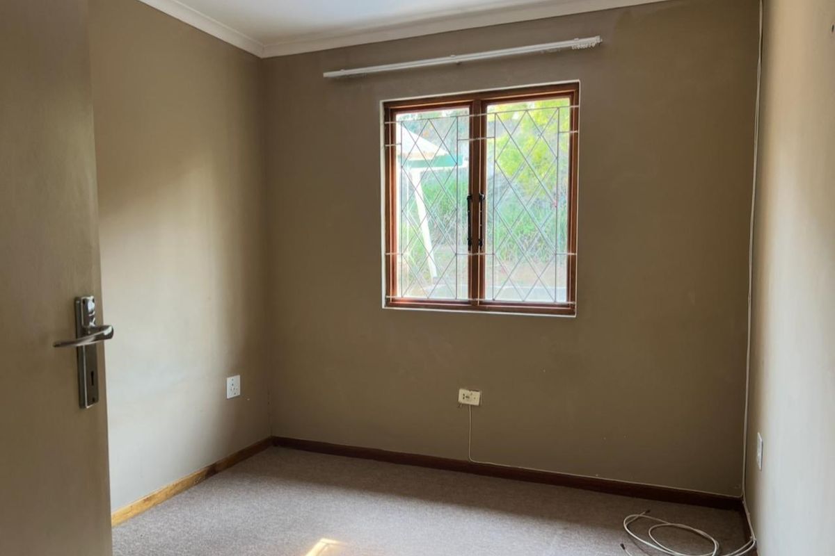 An empty bedroom featuring neutral wall tones, carpeted flooring, and a timber-framed window with security bars.