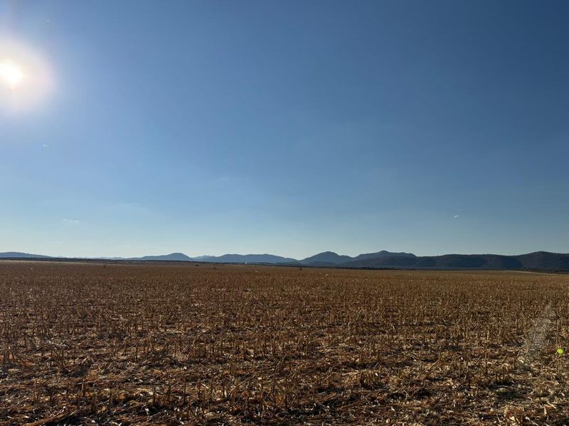 Expansive view of open farmland with distant mountain ranges under a clear blue sky.