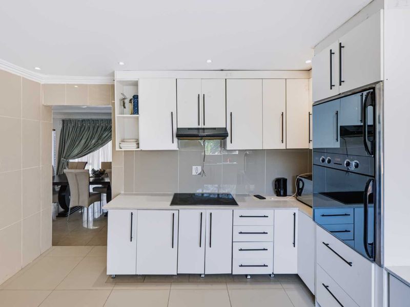 Modern kitchen featuring white cabinetry, sleek black hardware, integrated oven, electric hob, and neutral tiled finishes with a seamless flow to the dining area.