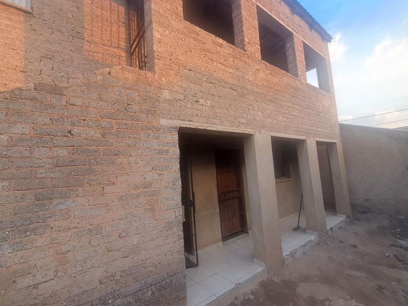 Two-story residential structure featuring exposed brickwork, concrete pillars, and a tiled ground-floor porch area, currently in an unfinished state.