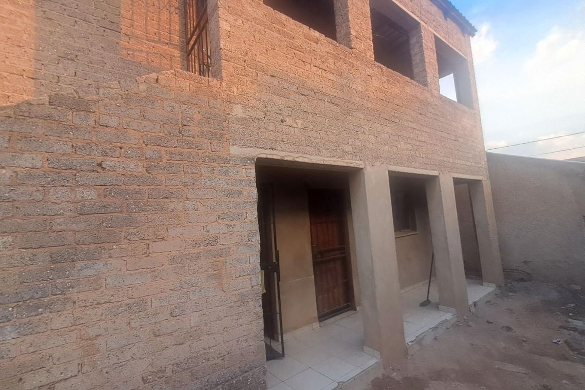 Two-story residential structure featuring exposed brickwork, concrete pillars, and a tiled ground-floor porch area, currently in an unfinished state.