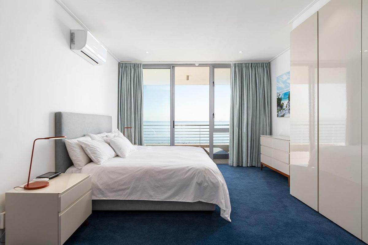 A bright, well-maintained bedroom featuring a built-in wardrobe, split-system air conditioning, and direct access to a balcony with ocean views.