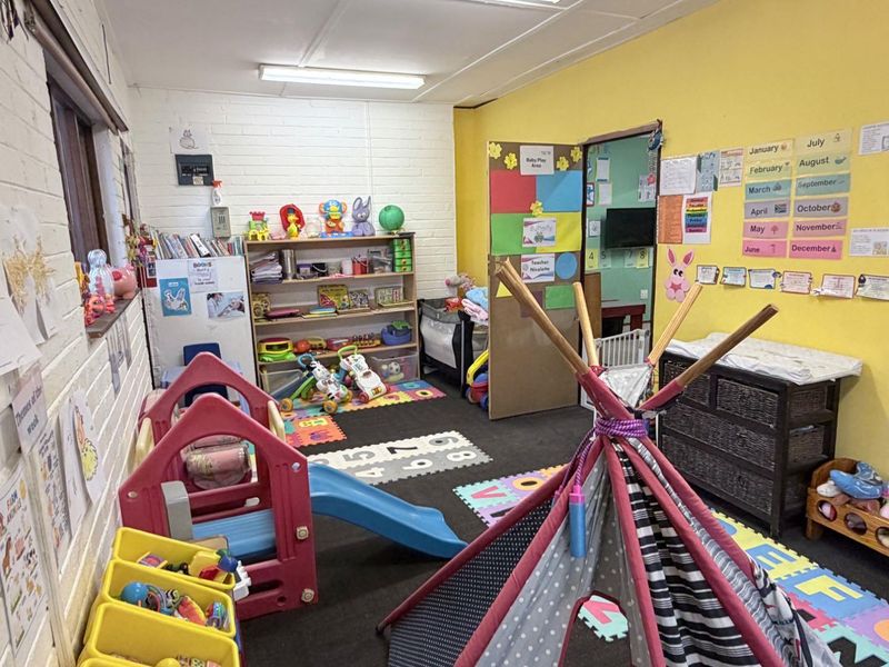 A functional utility space currently utilized as a childcare or play area, featuring painted brick walls and overhead fluorescent lighting.