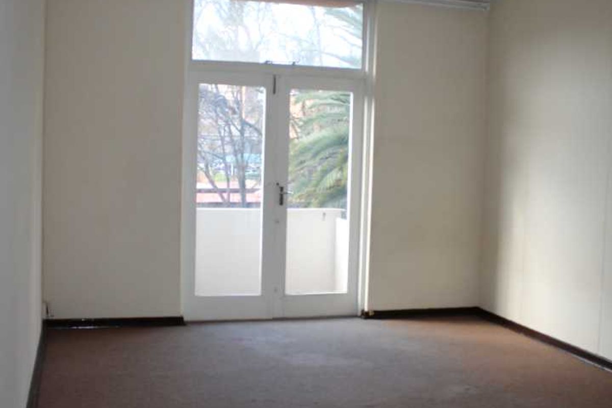 An empty living room featuring carpet flooring, a pendant light, and double glass doors leading to an outdoor balcony area.