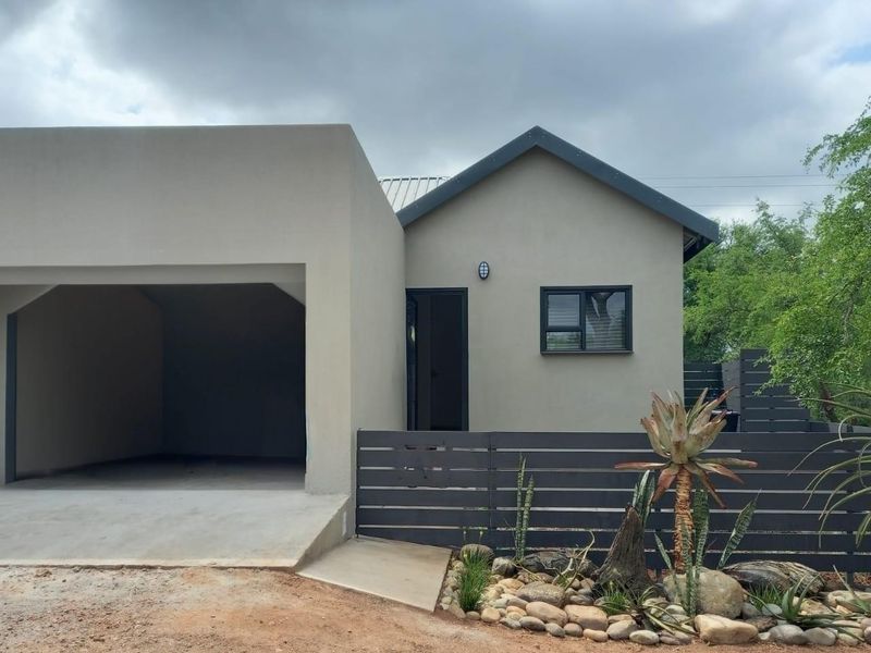 Modern single-story house exterior featuring a spacious garage, clean rendered facade, and contemporary horizontal slat fencing with landscaped garden beds.