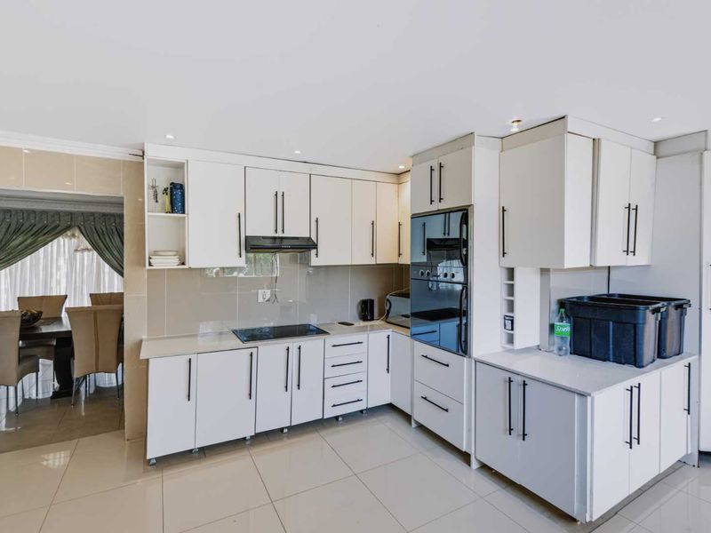 Modern kitchen featuring white cabinetry, stone countertops, integrated oven, electric hob, and sleek tiled flooring, offering a clean and functional culinary space.