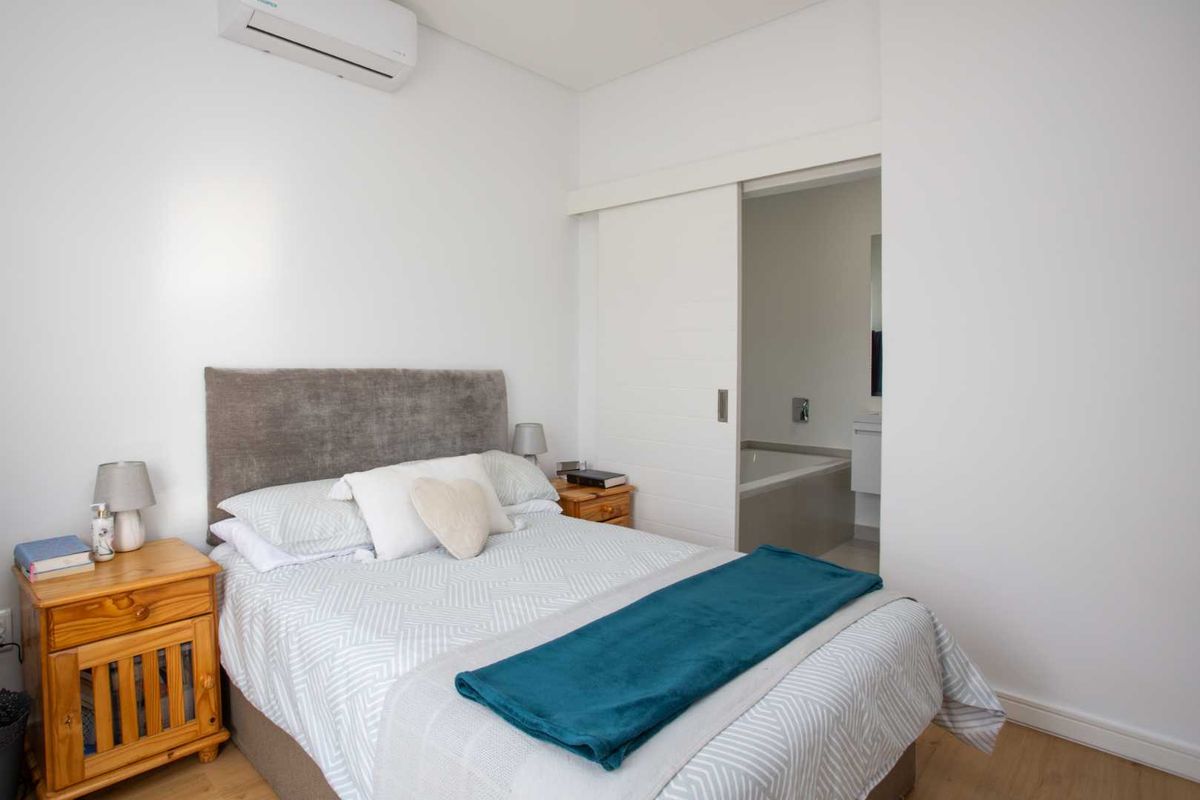 A well-maintained bedroom featuring laminate flooring, a wall-mounted air conditioning unit, and a sliding door providing direct access to an en-suite bathroom.