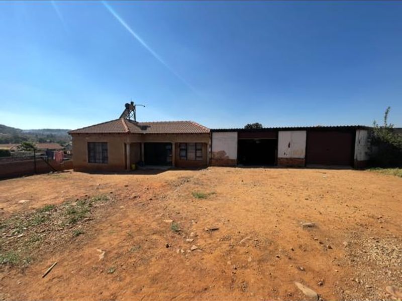Front exterior view of a single-story house featuring a tiled roof, solar water heater, and an attached double garage on a large unlandscaped plot.