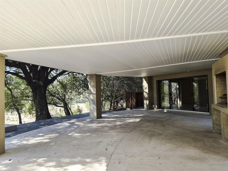 Spacious covered patio featuring concrete flooring, support columns, and a built-in outdoor braai, offering direct access to the interior through sliding glass doors.