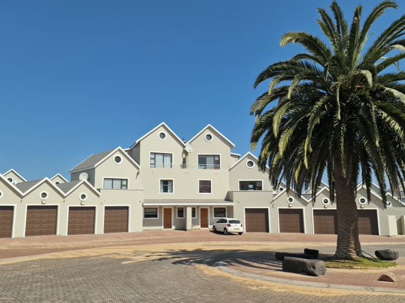 Front elevation of a townhouse complex featuring multiple garage doors, paved driveway, and gabled roof architecture.