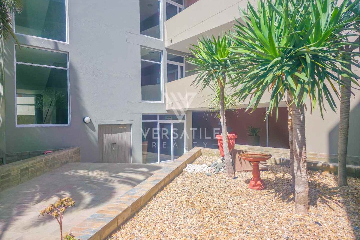 A view of the apartment building's exterior rear courtyard, featuring paved areas, gravel landscaping, and access to the ground floor units.
