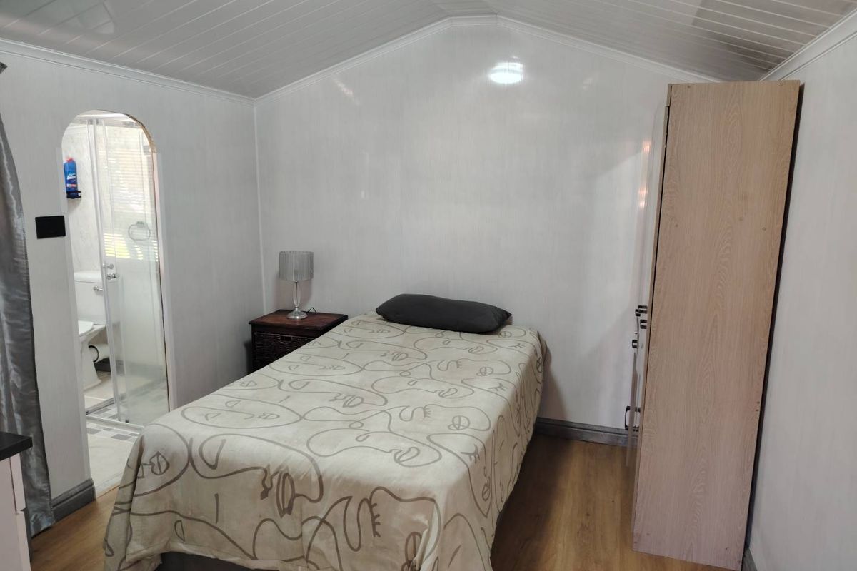 A compact bedroom featuring laminate flooring, a paneled ceiling, and an arched doorway leading to an en-suite bathroom.