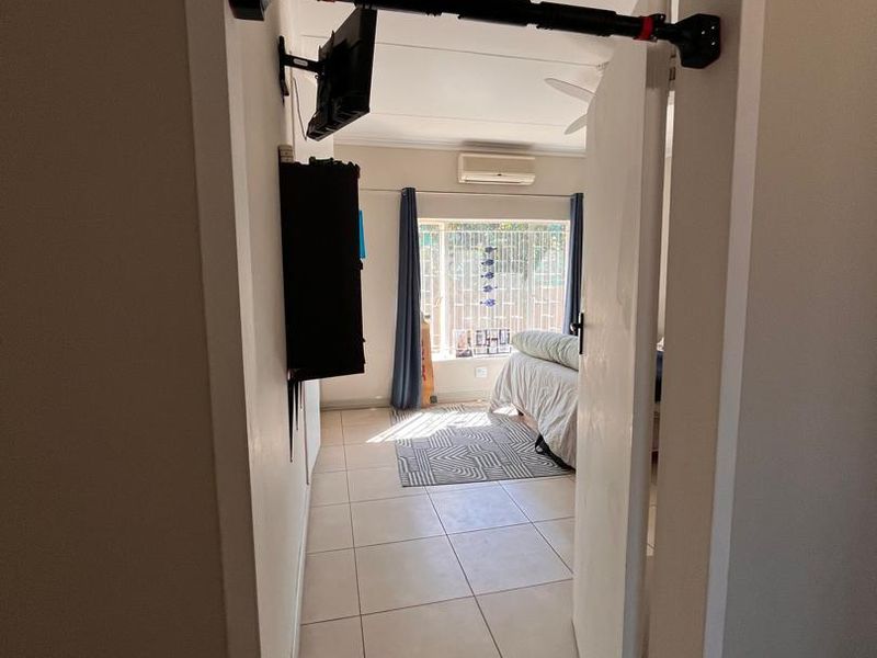 A bedroom featuring tiled flooring, a wall-mounted air conditioning unit, and a window fitted with security bars.