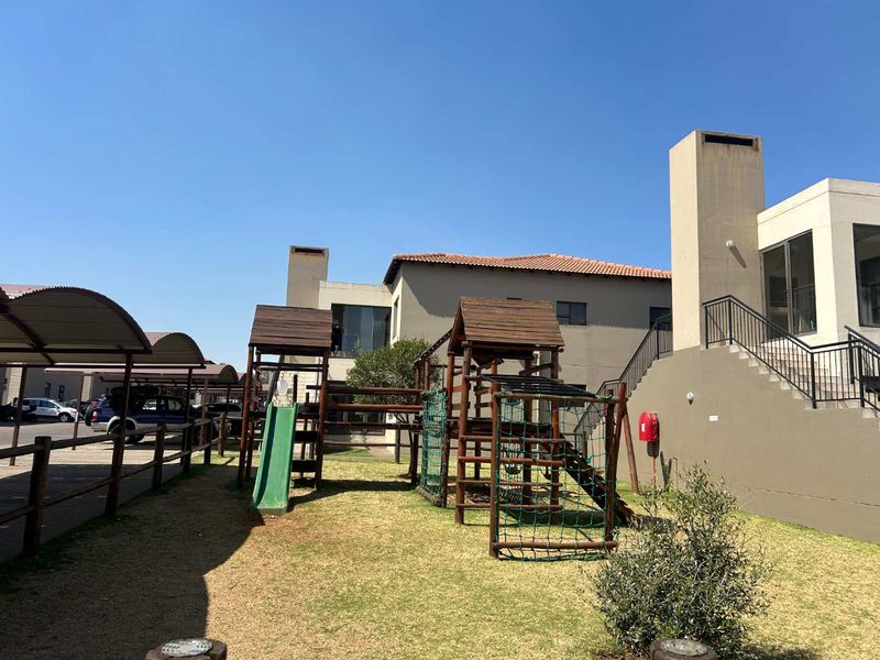 Communal outdoor area featuring a playground, paved parking area with carports, and exterior staircase access to the townhouse units.