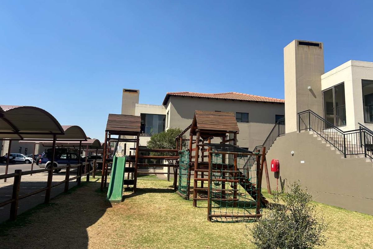 Communal outdoor area featuring a playground, paved parking area with carports, and exterior staircase access to the townhouse units.