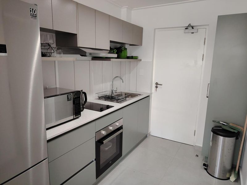 Modern galley-style kitchen featuring sleek grey cabinetry, stone countertops, integrated oven, electric hob, and a stainless steel sink with a contemporary mixer tap.