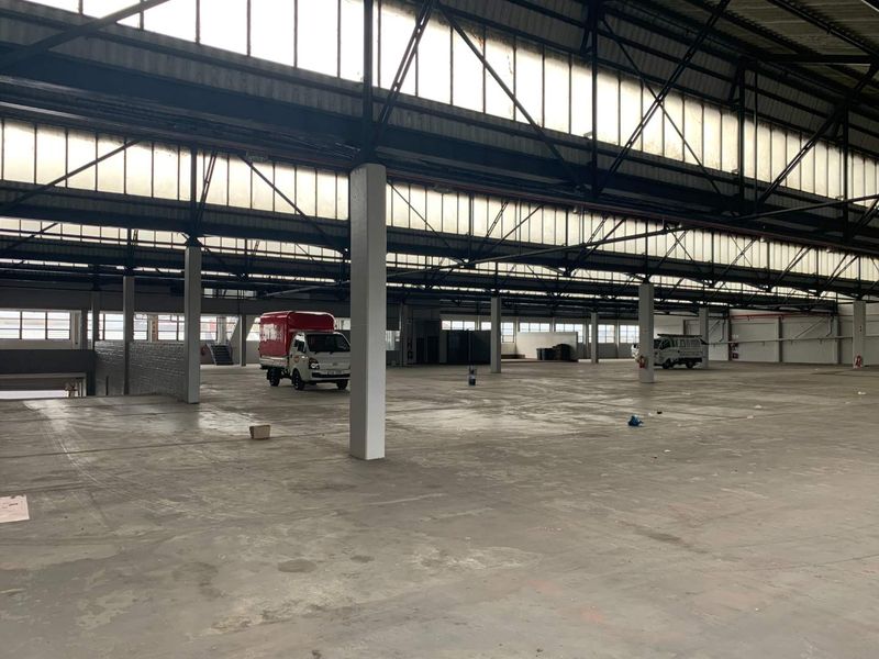 Expansive industrial warehouse space featuring high ceilings, steel truss roofing, abundant natural light from clerestory windows, and durable concrete flooring.
