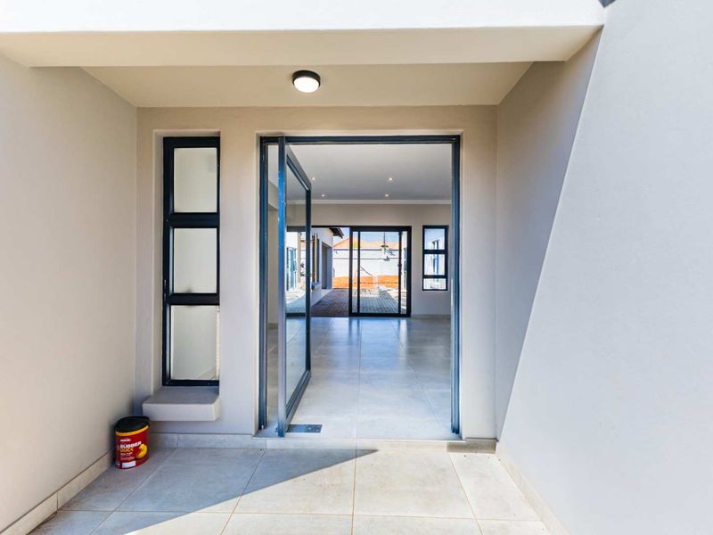 A modern, clean entrance area featuring a large glass pivot door, neutral tiled flooring, and contemporary aluminium window frames.