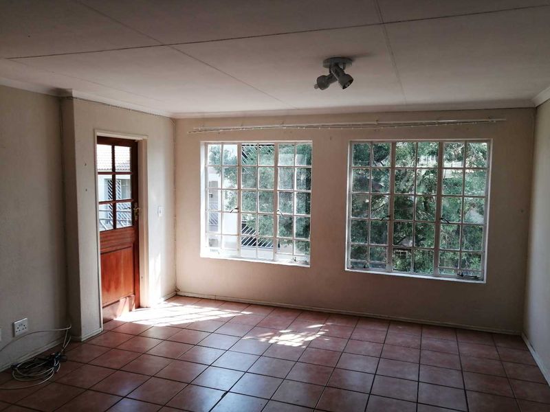 An empty living room featuring tiled flooring, large multi-pane windows, and a timber-framed glass door leading to an exterior area.