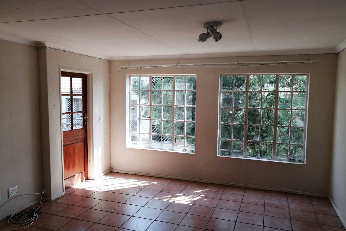An empty living room featuring tiled flooring, large multi-pane windows, and a timber-framed glass door leading to an exterior area.