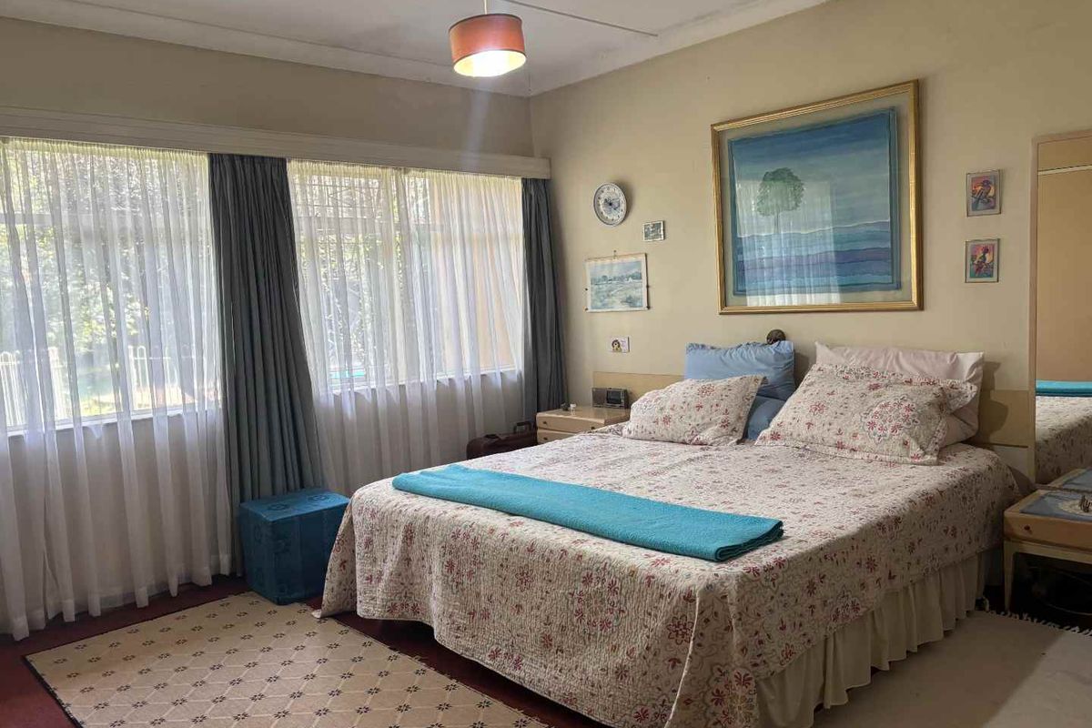 A spacious bedroom featuring large windows with natural light, neutral wall tones, and carpeted flooring, offering a comfortable and functional living space.