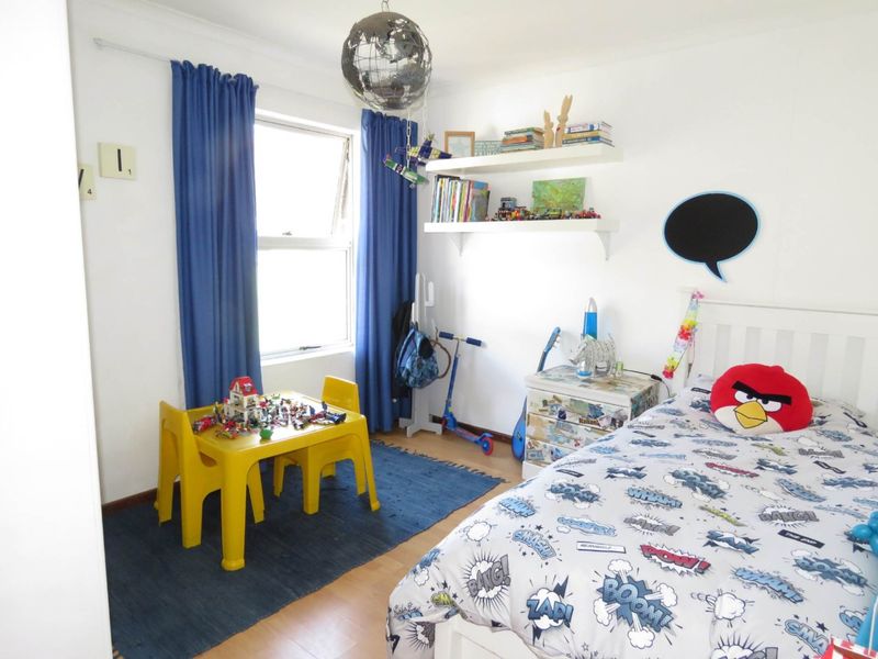 A bright bedroom featuring laminate flooring and a functional casement window, providing a comfortable space with built-in shelving for storage.