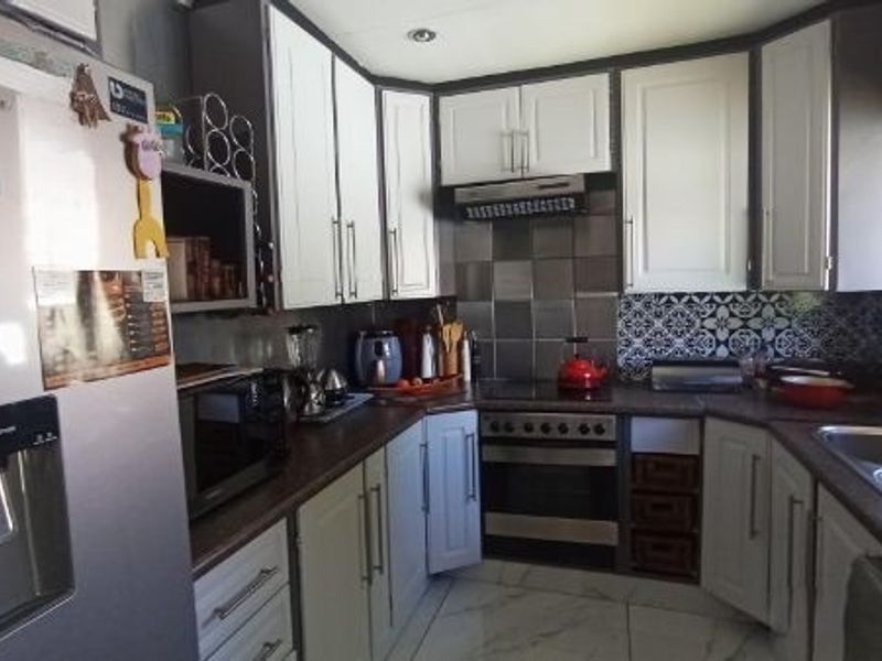 A functional kitchen featuring two-tone cabinetry, laminate countertops, a built-in oven with extractor fan, and a double bowl sink with decorative tiled backsplash.
