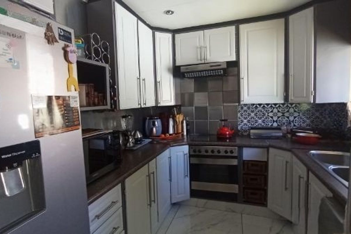 A functional kitchen featuring two-tone cabinetry, laminate countertops, a built-in oven with extractor fan, and a double bowl sink with decorative tiled backsplash.