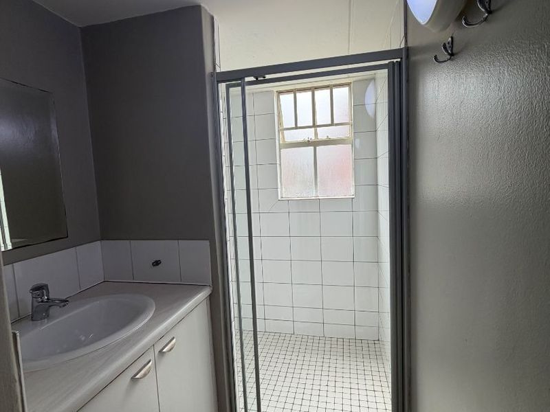 A functional bathroom featuring a vanity with basin, a separate shower enclosure with tiled finishes, and a wall-mounted light fixture.