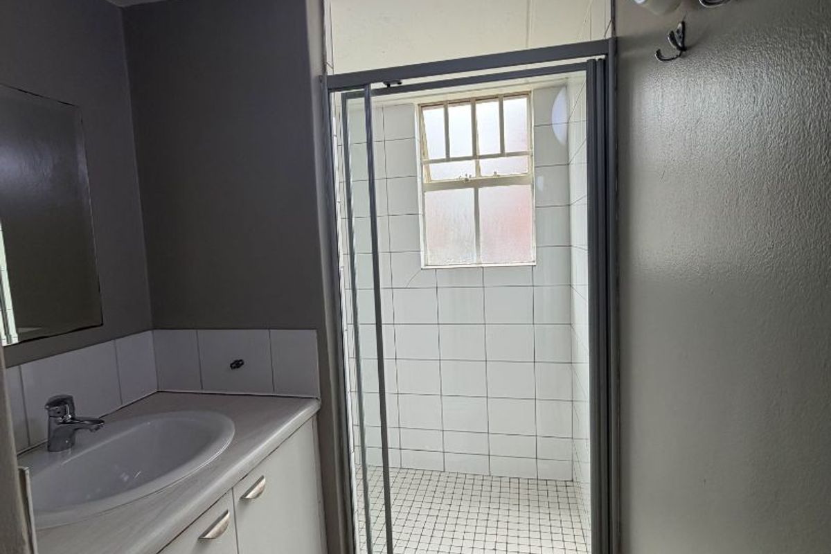 A functional bathroom featuring a vanity with basin, a separate shower enclosure with tiled finishes, and a wall-mounted light fixture.